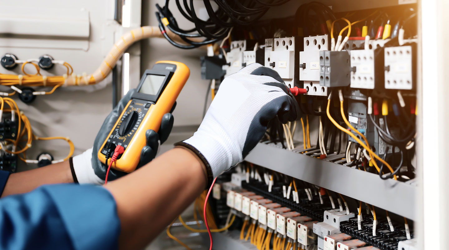 Technicien en tenue de sécurité inspectant une armoire électrique dans un couloir technique de site industriel