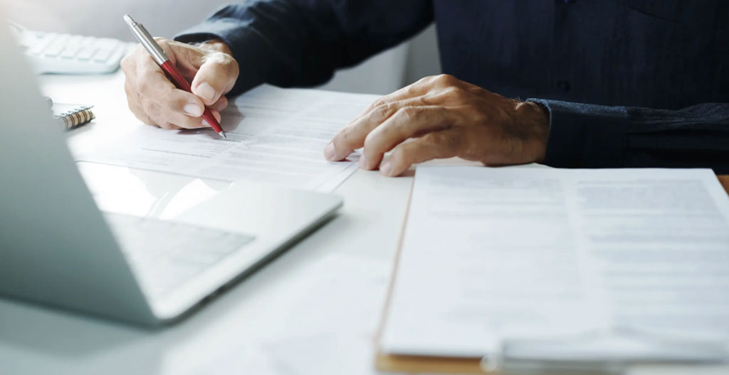 Gros plan sur des mains consultant et surlignant attentivement les clauses d'un contrat d'électricité professionnel, avec conditions générales étalées sur un bureau